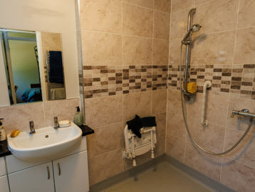 Accessible walk-in shower with sandy-coloured tiles, sink and mirror in a modern bathroom