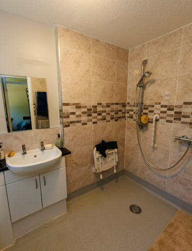 Accessible walk-in shower with sandy-coloured tiles, sink and mirror in a modern bathroom 