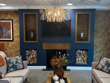 A communal lounge with light grey sofas, a coffee table and a log fire.