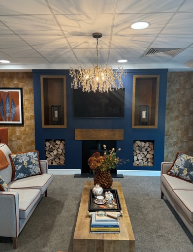 A communal lounge with light grey sofas, a coffee table and a log fire. 