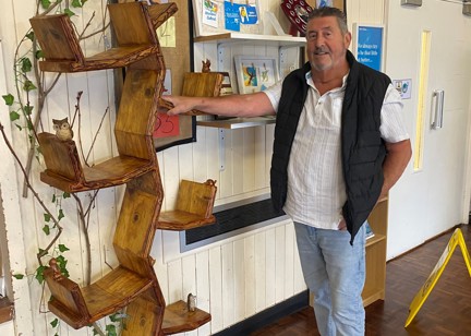Dave, the carpenter, stands beside his handcrafted wooden bookcase