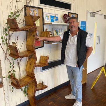 Dave, the carpenter, stands beside his handcrafted wooden bookcase