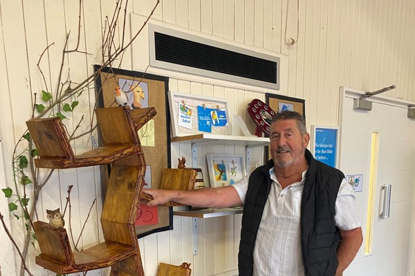Dave, the carpenter, stands beside his handcrafted wooden bookcase