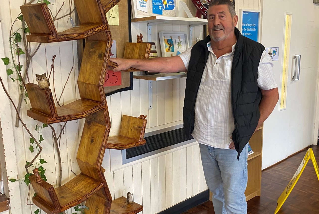 Dave, the carpenter, stands beside his handcrafted wooden bookcase