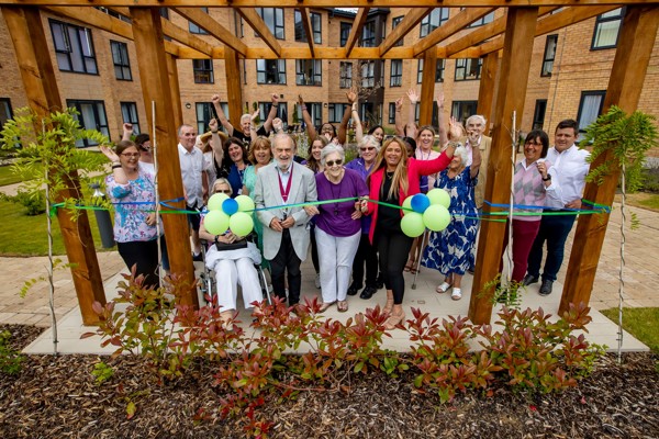 The grand opening of Poppy Meadows with a group of people outside cutting the ribbon with balloons