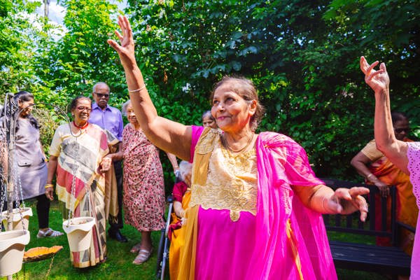 Resident wearing a pink sari dress, dancing in a garden with other residents watching
