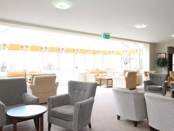 Inside the bright residents lounge with soft seating, tables and conservatory