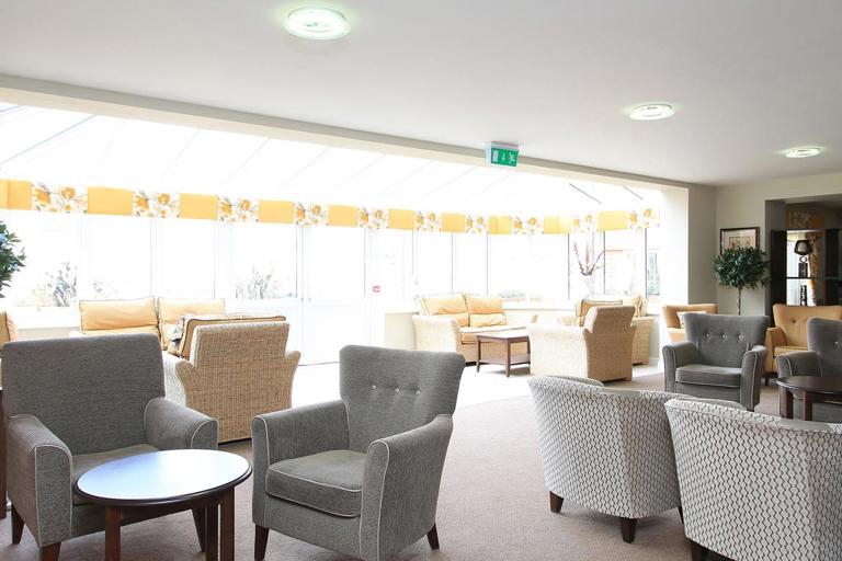 Inside the bright residents lounge with soft seating, tables and conservatory