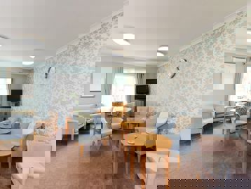 Soft seating and tables in a residents' lounge with TV on a small unit in the corner