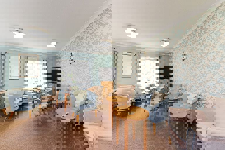 Soft seating and tables in a residents' lounge with TV on a small unit in the corner