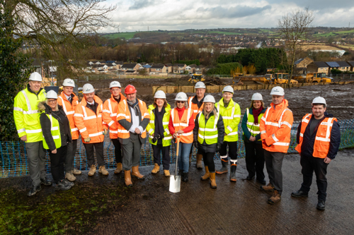 Key representatives from Housing 21, Kirklees Council, and Robertson Group, standing outside in high vis jackets and hard hats holding a spade at the Cleckheaton Extra Care scheme ground-breaking ceremony