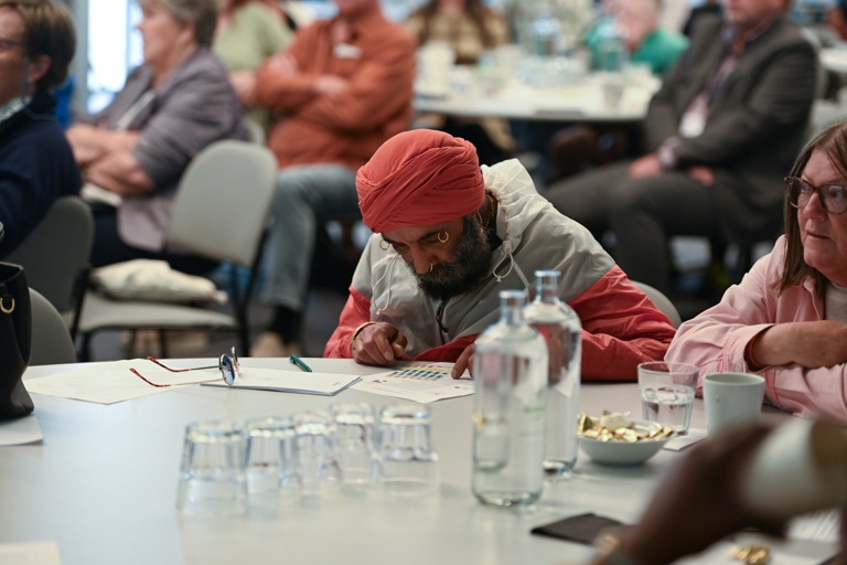 Man wearing peach coloured turban studies paperwork on a table