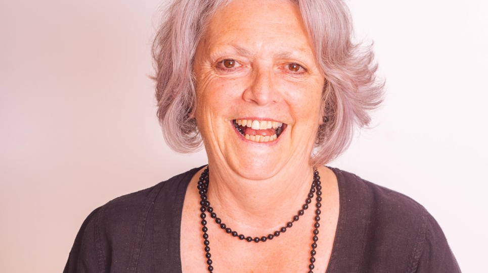 Resident with grey hair and wearing a black outfit holding a walking stick and smiling at the camera