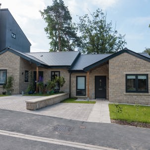 An image showing the outside of a bungalow at Bowland View. The bungalow features a patio with a small grassed area