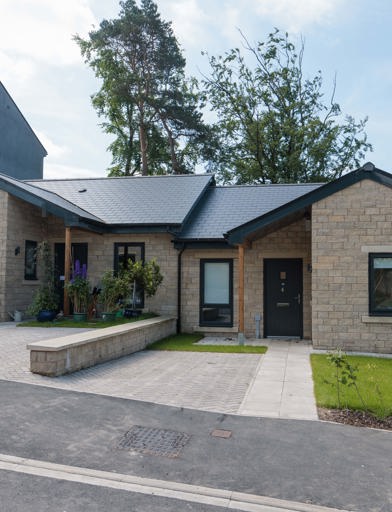 An image showing the outside of a bungalow at Bowland View. The bungalow features a patio with a small grassed area