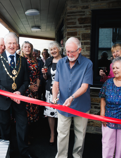 An older man in a blue shirt, cuts a red ribbon to open Lowarth Morbies 