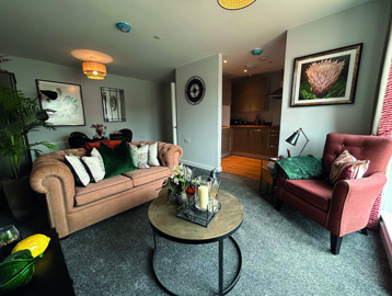 A living room inside an apartment at Askern Vale featuring a dining table with chairs, sofa and a single sofa chair with a coffee table in the middle