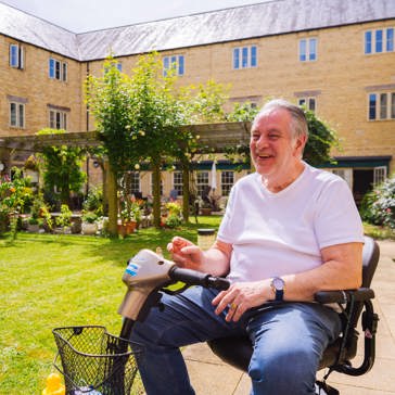 Resident in a wheelchair in a communal garden on a sunny day smiling