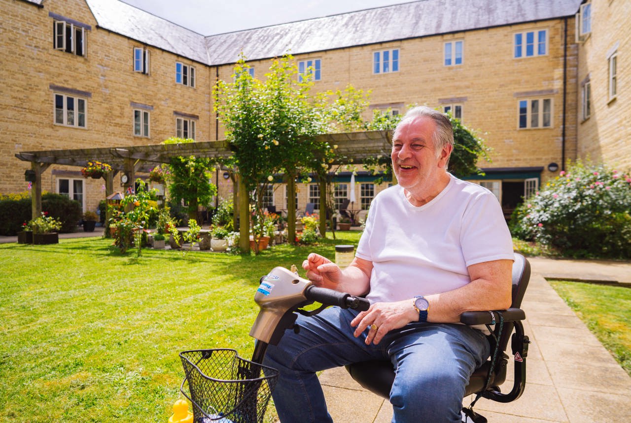 Resident in a wheelchair in a communal garden on a sunny day smiling