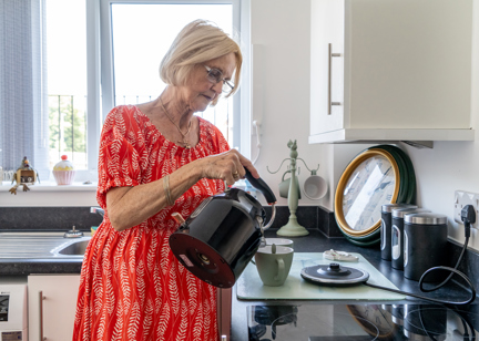 Resident in a red dress pouring a kettle of hot water into a cup in the kitchen of their apartment