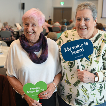 Two female residents hold signs that say 'my voice is heard' and 'people listen to me'