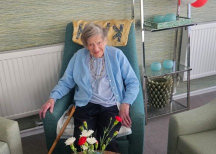 Lady sits in armchair with red flowers in vase