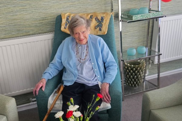 Lady sits in armchair with red flowers in vase