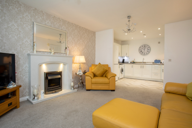 Spacious open-plan apartment featuring a lounge with comfortable seating, fireplace and television, leading into a modern fitted kitchen with integrated appliances.