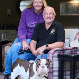 A couple who are residents smiling with their dog in the communal lounge