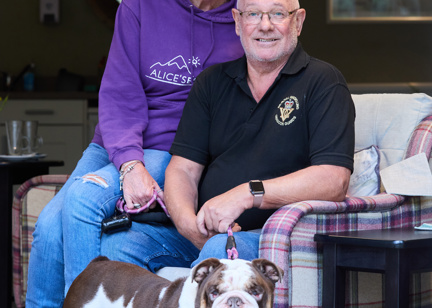 A couple who are residents smiling with their dog in the communal lounge