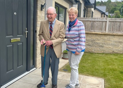 Resident John smiling standing next to his daughter Jackie, outside the front of his bungalow