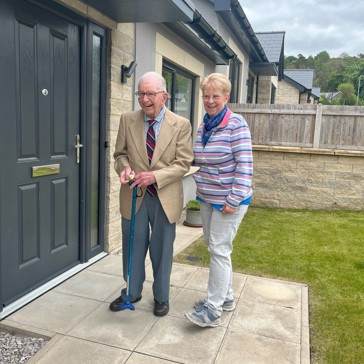 Resident John smiling standing next to his daughter Jackie, outside the front of his bungalow