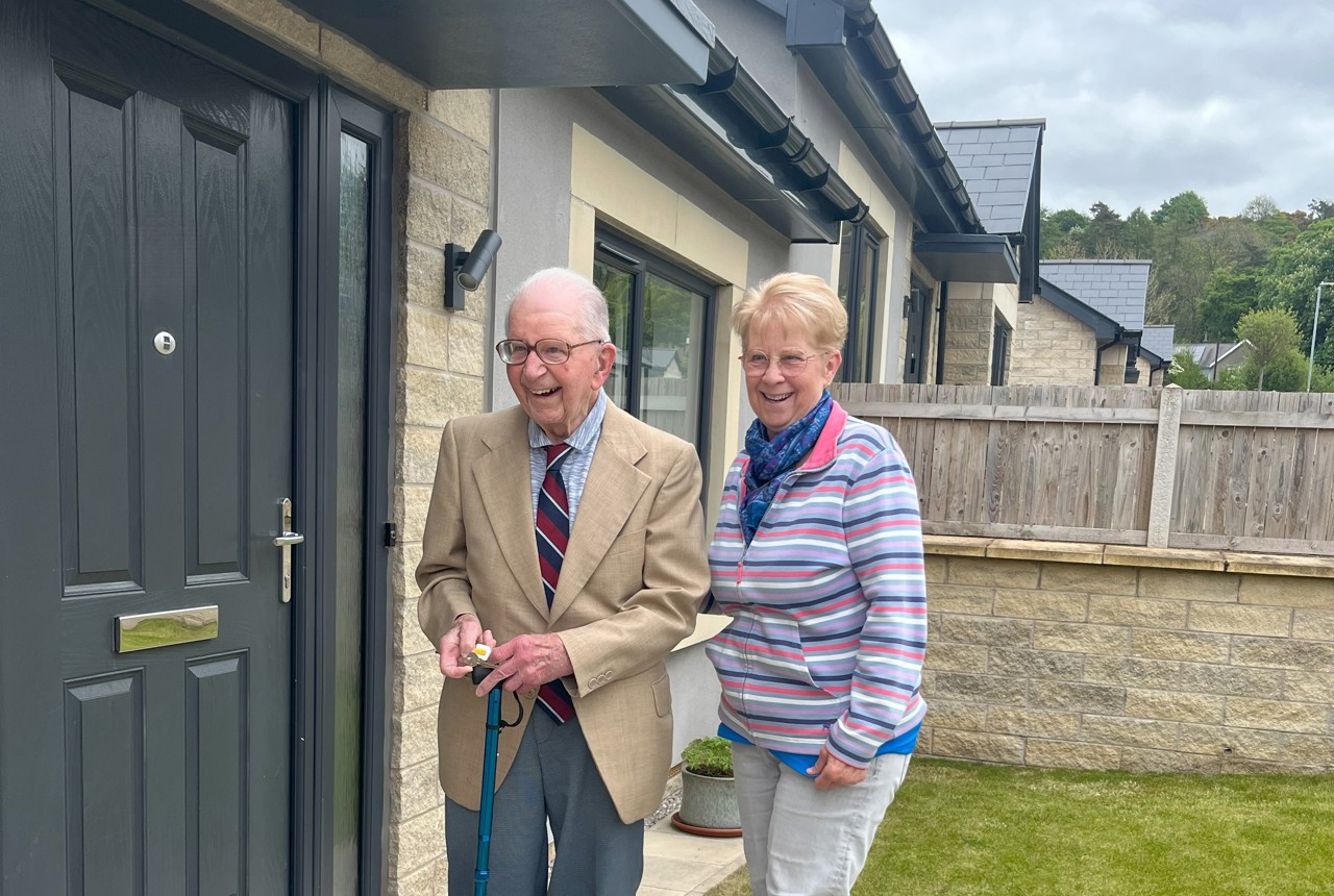 Resident John smiling standing next to his daughter Jackie, outside the front of his bungalow