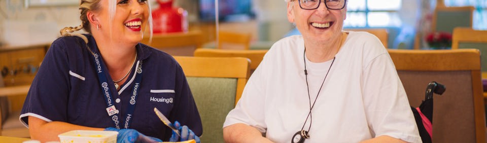 A Care Worker buttering some toast for a resident whilst they are sat together at a table 