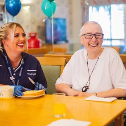 A Care Worker buttering some toast for a resident whilst they are sat together at a table