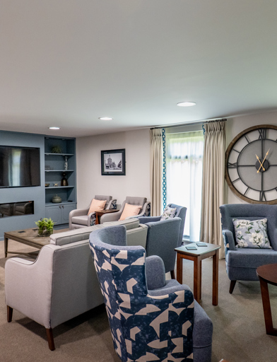 William Griffiths Court internal shot: Television area with a selection of seating chairs and sofas, decorated with a large clock and potted plants 