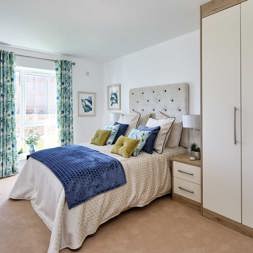 A bedroom furnished with a bed, wardrobe, side table and chest of drawers with a full length window to the rear