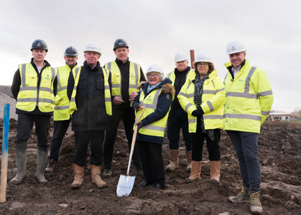 People wearing hard hats and one lady carries a spade