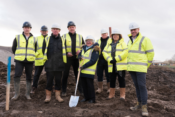 People wearing hard hats and one lady carries a spade