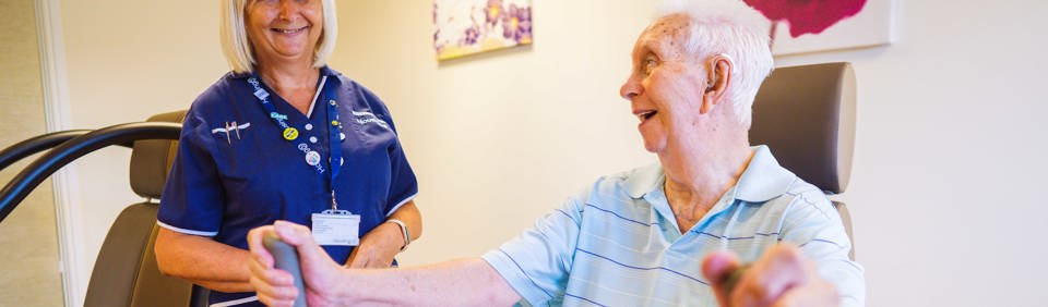 An Extra Care resident using gym equipment with help from a carer from Housing 21 
