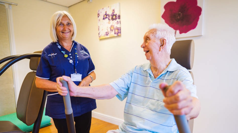 An Extra Care resident using gym equipment with help from a carer from Housing 21