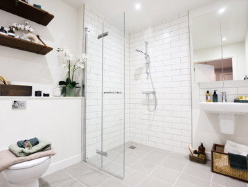 Inside the wet-room style bathroom of a show apartment at Minterne Apartments with white tiles