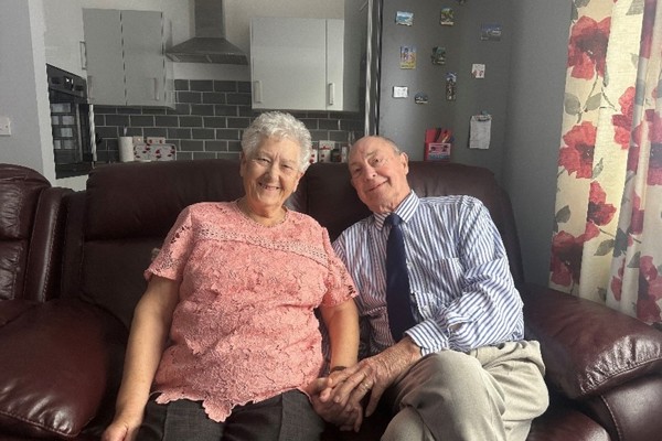 Vinnicombe Court residents David and Shirley sitting together on a sofa holding hands. 