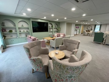A communal seating area with armchairs and sofas with a large TV on the wall