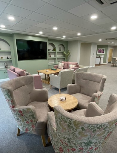 A communal seating area with armchairs and sofas with a large TV on the wall
