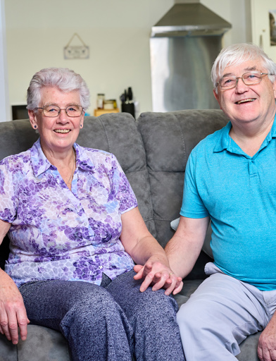 A couple holding hands while sat in their modern, bright living room 