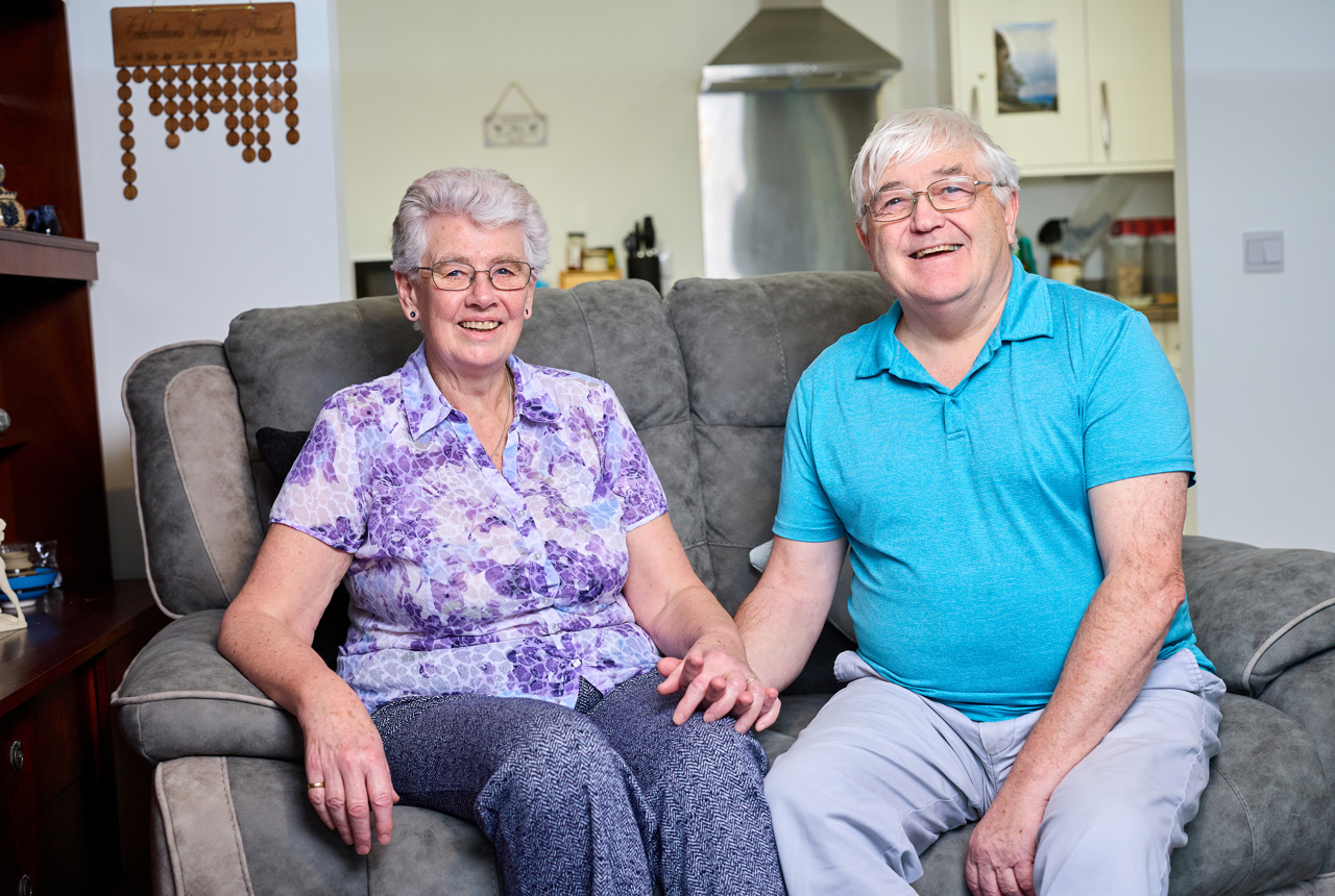 A couple holding hands while sat in their modern, bright living room