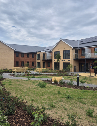 Landscape image showing the building of Extra Care scheme Michaelmas Court, with grass and tree's in front of the building 