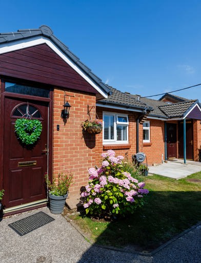 A row of bungalows with flowers and hanging baskets around the front door 