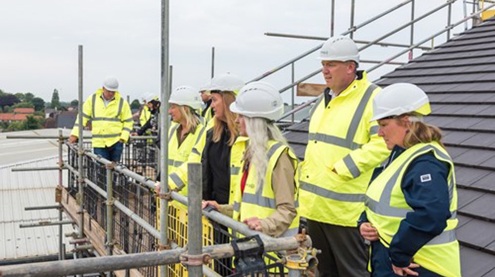 Housing 21 employees and stakeholders wearing high vis gather at the site of the Aldaniti Court development